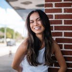 A young woman with long hair smiles while leaning against a red brick wall in Orlando, Florida.