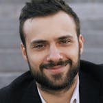 Close-up of a smiling man in a suit sitting outdoors on steps.